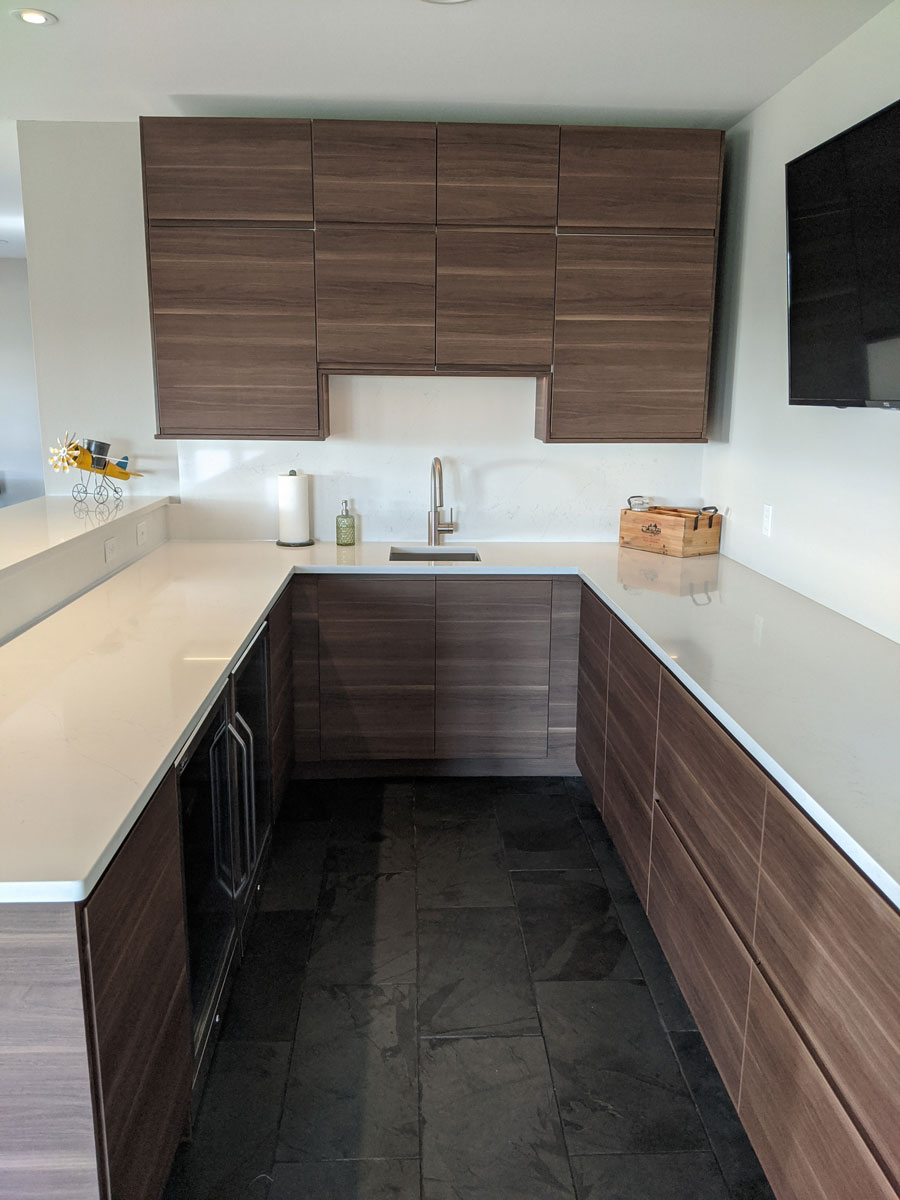 Warm-toned IKEA VOXTORP kitchenette with under-cabinet lighting, walnut doors, and a two-tier bar seating area.
